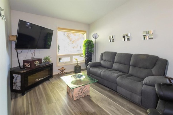 Living room with a dark gray sectional sofa, glass coffee table, and wall-mounted TV. - 7 Gimli Place, Winnipeg