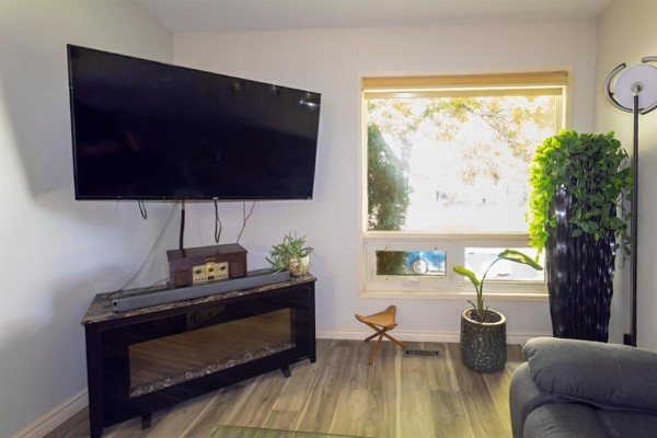 Living room showing a wall-mounted TV, entertainment unit, large window, and potted plants. - 7 Gimli Place, Winnipeg