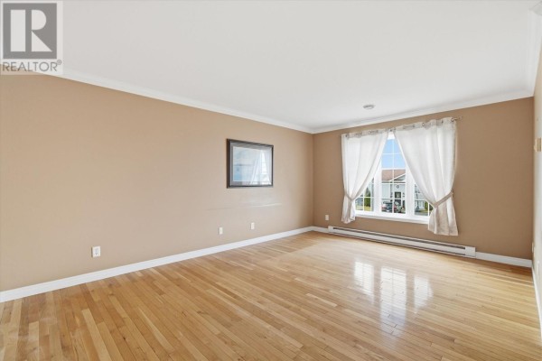 Empty living room with light hardwood floors, beige walls, and white curtains on a large window. - 7 Irish Loop Street, St  John S