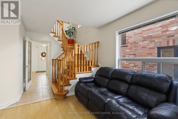 Living room with a black leather sofa, hardwood floors, and a wooden staircase. - 7 Isabella Garden Lane, Whitchurch Stouffville