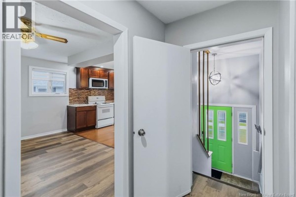 Hallway view showing a bright green front door and stairs, with a kitchen visible through an opening. - 7 James Street, Moncton