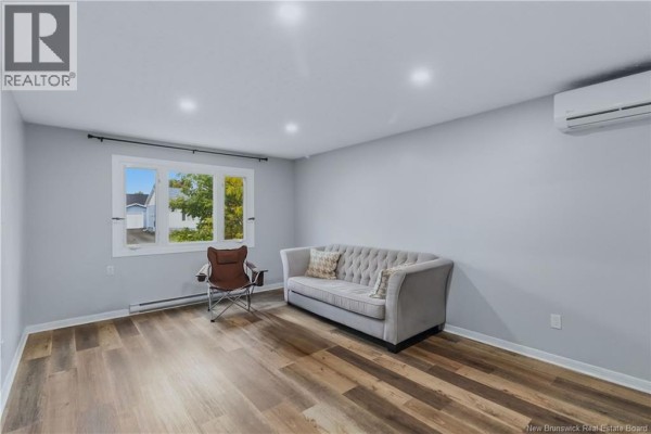 Living room with light grey walls, a large window, a grey tufted sofa, and a brown armchair. - 7 James Street, Moncton