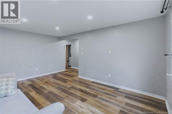 Living room with light grey walls, wood-look flooring, and an opening to a hallway. - 7 James Street, Moncton