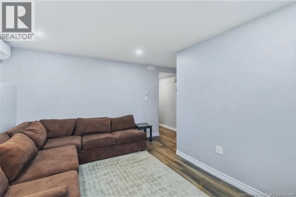 Living room with light grey walls, wood-look flooring, and a large brown sectional sofa on a rug. - 7 James Street, Moncton
