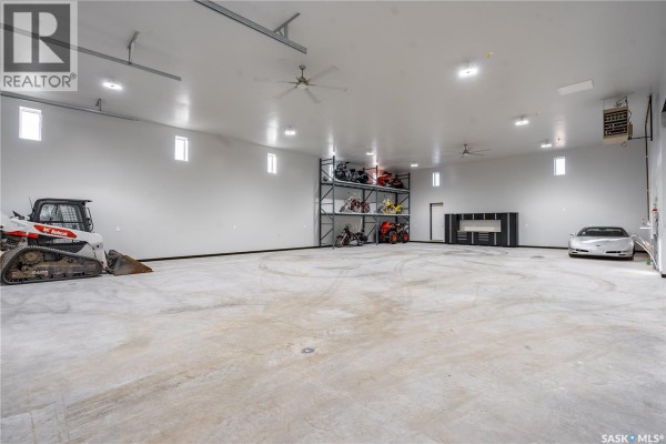 Expansive white garage interior with concrete floor, multiple vehicles, and storage shelves. - 7 Loewen Court, Warman
