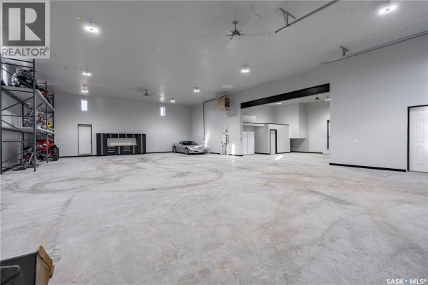 Spacious white garage interior with concrete floor, vehicles, and doorway leading to another area. - 7 Loewen Court, Warman