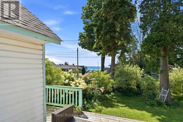 Exterior of a white cottage with light blue trim, featuring a wooden deck and surrounding greenery. - 7 Oliver Drive, Tiny