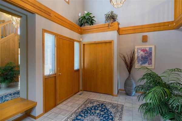 Foyer with tile floor, wood trim, double closet, and staircase leading upstairs. - 7 Princemere Road, Winnipeg