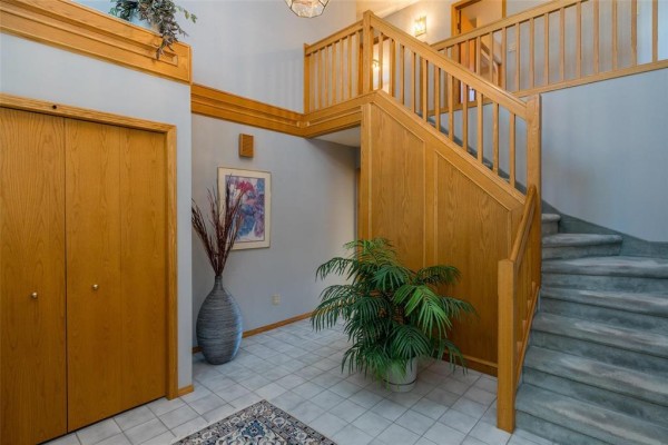Foyer with double wood doors, staircase, potted plant, and artwork on the wall. - 7 Princemere Road, Winnipeg
