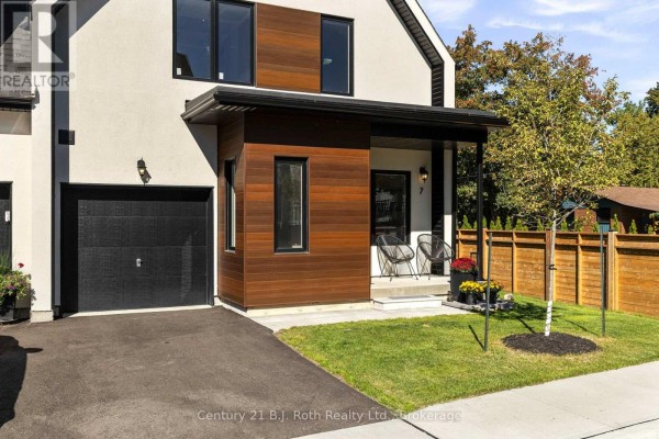View of the townhouse entrance and garage with wood siding accents, gray pavement, and a landscaped lawn. - 7 Rice Lane Road, Orillia