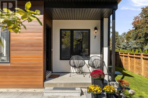 Front porch of the townhouse with two chairs, potted flowers, and a number 7 above a window. - 7 Rice Lane Road, Orillia