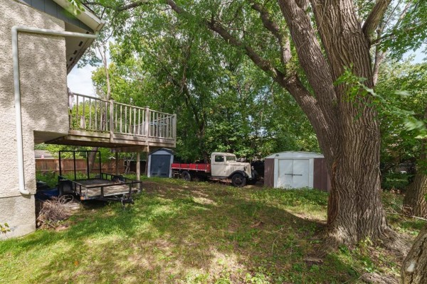 Rear exterior of the house with a raised wooden deck, view of a vintage truck and trailers on the overgrown lawn. - 7 Scotswood Drive, Winnipeg