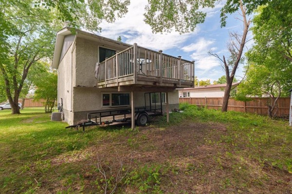 Backyard view showing a wooden deck, trailers, and two storage sheds, with mature trees providing shade. - 7 Scotswood Drive, Winnipeg