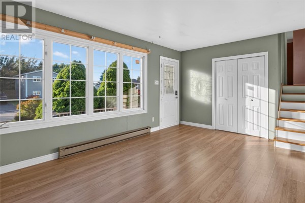 Living room with wide windows, green walls, double white doors, and stairs. - 7 Scott Place, Gander
