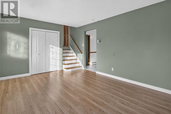 Living room with green walls, laminate flooring, white double doors, and stairs leading up. - 7 Scott Place, Gander