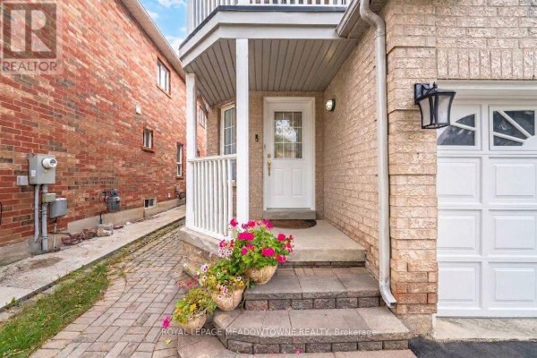 Close-up of a townhouse entrance with a white door, stone steps, and potted pink flowers. - 7 Secord Crescent, Brampton