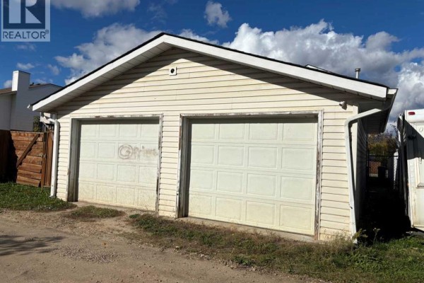 Detached two-car garage with white paneled doors and light beige siding. - 7 Steward Drive, Whitecourt