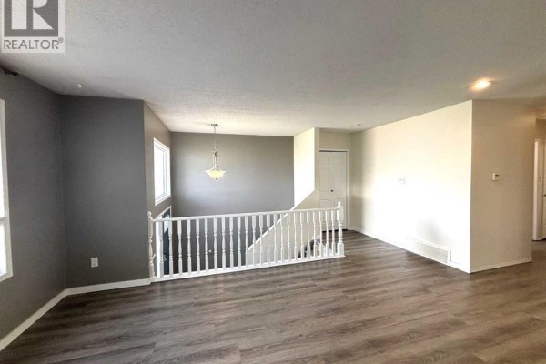 Living area with grey accent wall, white railing, and dark wood laminate flooring. - 7 Steward Drive, Whitecourt