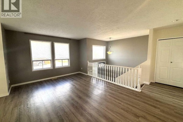 Living room with grey walls, large windows, and white banister overlooking staircase. - 7 Steward Drive, Whitecourt