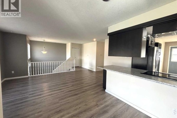 Kitchen area with dark cabinets, granite countertops, and view of living room and stairs. - 7 Steward Drive, Whitecourt