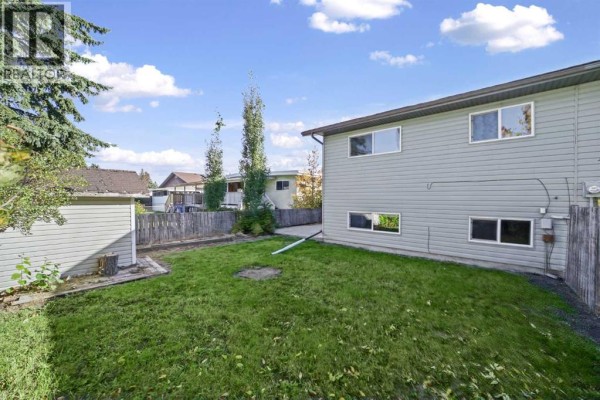Rear view of the duplex with a lawn, shed, and trees. A wooden fence borders the property. - 7 Westhill Place, Didsbury