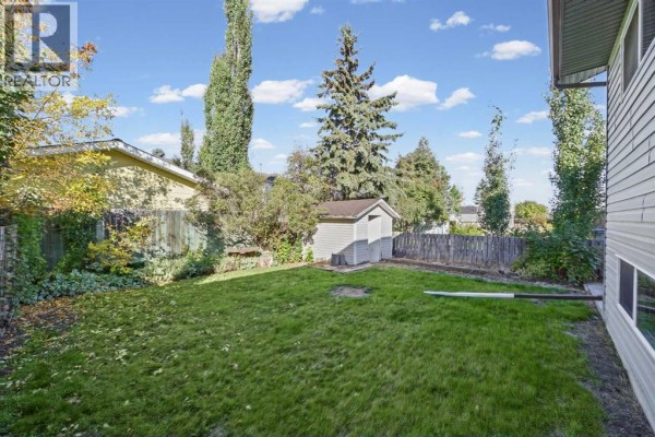 Spacious backyard of the duplex with a lawn, shed, and mature trees. The house siding is light grey. - 7 Westhill Place, Didsbury