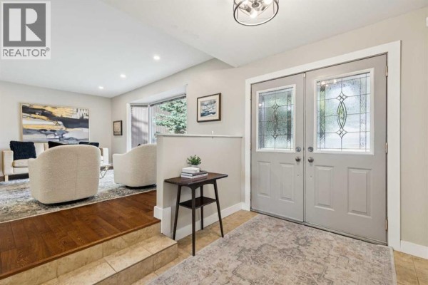 Foyer with double glass doors, tiled floor, and a raised living area with hardwood floors. - 7 Woodgreen Crescent Sw, Calgary