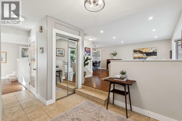 Interior view of the foyer, leading to a sunken living room and a hallway with mirrored closet doors. - 7 Woodgreen Crescent Sw, Calgary