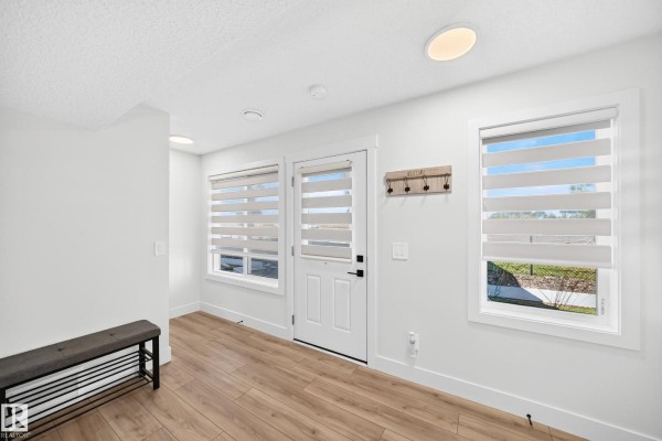 Bright entryway with white walls, wood-look flooring, a white door, and two windows with blinds. - #70 16335 84 St Nw, Edmonton