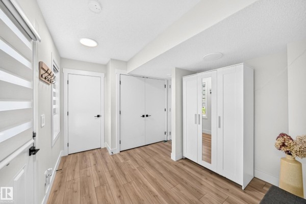 Hallway inside a townhouse with white walls, wood-look flooring, a white closet, and two white doors. - #70 16335 84 St Nw, Edmonton