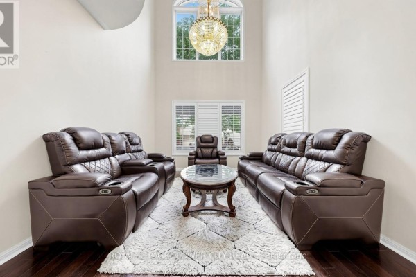Living room with dark leather sofas, a coffee table, shag rug, and a grand chandelier. - 70 Boom Road, Vaughan
