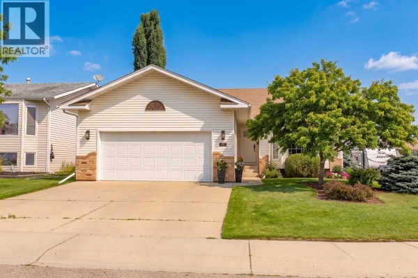 Front exterior of a beige vinyl-sided house with a double garage door and a green lawn. - 70 Densmore Crescent, Red Deer