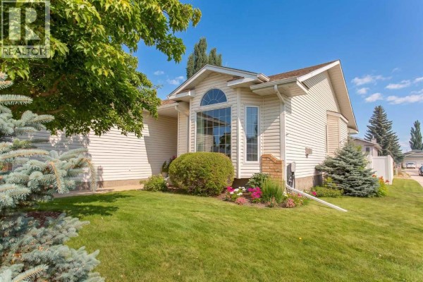 Side exterior of a beige vinyl-sided house with a bay window and manicured landscaping. - 70 Densmore Crescent, Red Deer