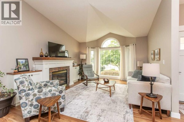 Living room with a fireplace, vaulted ceiling, large arched window, and seating. - 70 Densmore Crescent, Red Deer