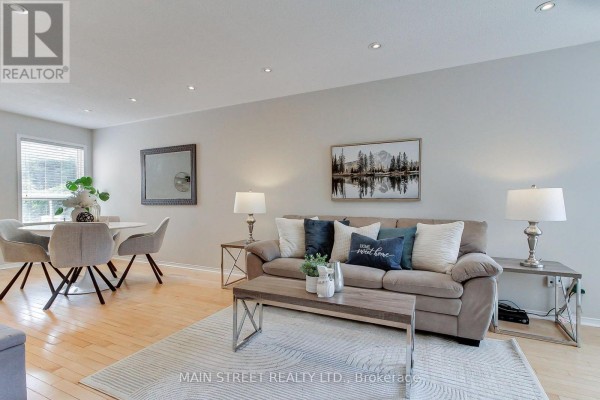 Living room with a sofa, coffee table, dining area, and hardwood floors. - 70 Dunsmore Crescent, Richmond Hill