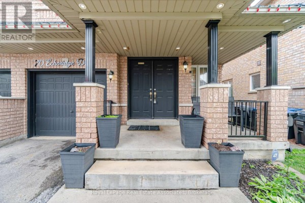 Entrance to a townhouse with a two-car garage, double front doors, and planters. - 70 Echoridge Drive, Brampton
