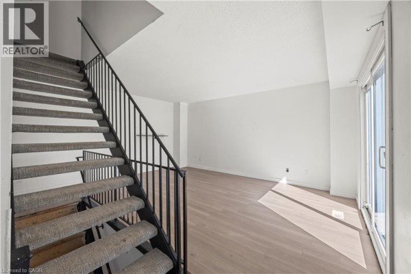 Interior living space with light wood floors, white walls, and a staircase with carpeted steps. - 70 Fiddlers Green Road Unit# 74, London