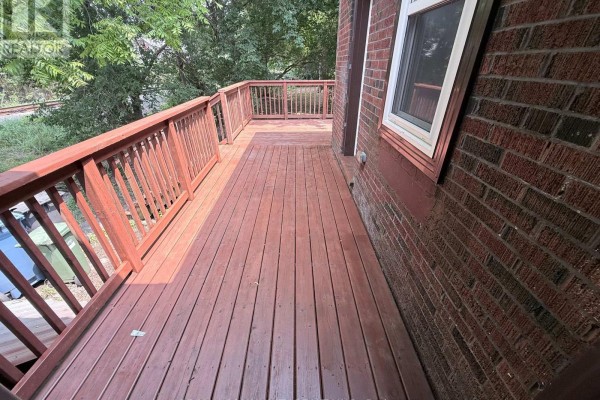 A long wooden deck with railings runs along the side of the brick house. - 70 Huron Street, Guelph
