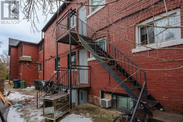 Front exterior of the multi-family home featuring stone facade and large arched window. - 70 Melbourne Avenue, Toronto