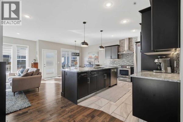 Open-concept kitchen with dark cabinets, a large island with granite countertops, and stainless steel appliances. - 70 Mitchell Crescent, Blackfalds