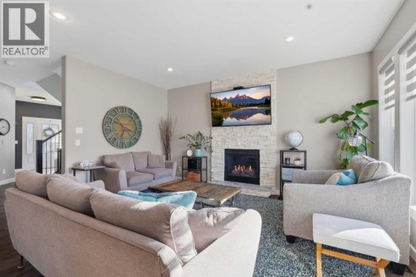 Living room with a stacked stone gas fireplace, a television, two sofas, and armchairs. - 70 Mitchell Crescent, Blackfalds