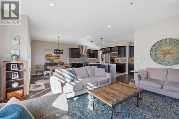 Living room and dining area with sofas, a coffee table, and a view of the kitchen and dining table. - 70 Mitchell Crescent, Blackfalds