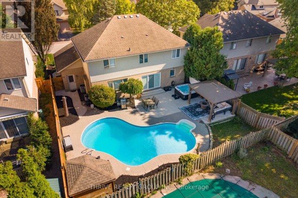 Aerial view of a backyard with a kidney-shaped swimming pool, hot tub, covered patio, and wooden fence. - 70 Pinebrook Court, London North