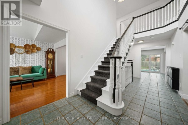 Interior view of a spacious foyer with a staircase, tiled floor, and an open doorway to a living room. - 70 Pinebrook Court, London North