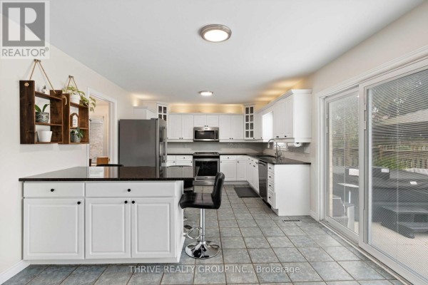 White kitchen with granite countertops, stainless steel appliances, a large island with bar stools, and tile flooring. - 70 Pinebrook Court, London North