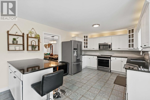 White kitchen with granite countertops, stainless steel appliances, a large island with bar stools, and tile flooring, looking towards dining room. - 70 Pinebrook Court, London North