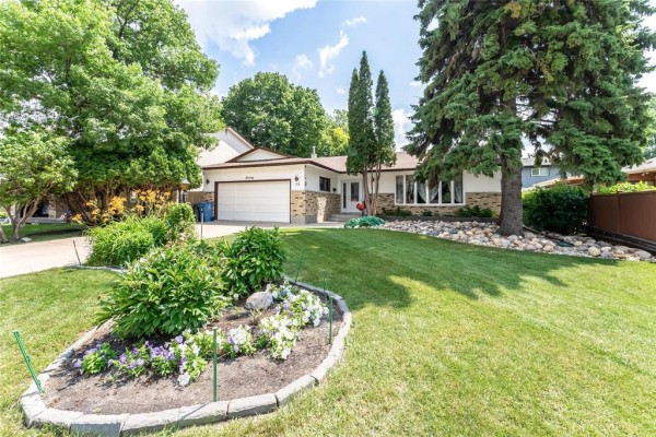 Front yard landscaping with a circular flower bed and green grass. - 70 Radcliffe Road, Winnipeg