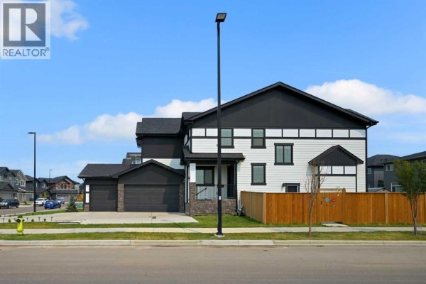 Side exterior view of the house showcasing the dark trim, white siding, and attached garage. - 70 South Shore Bay, Chestermere