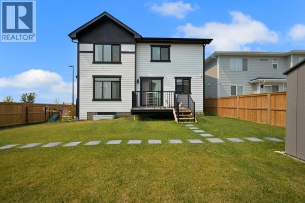 The backyard features a green lawn, a wooden deck with stairs, and stepping stones leading to a shed. - 70 South Shore Bay, Chestermere