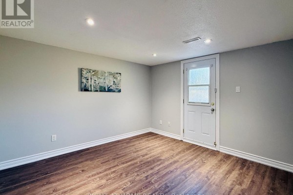 Empty room with dark wood flooring and a door leading outside. - 70 Spire Hillway Way, Toronto